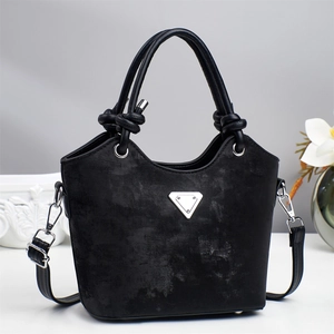 Minimalist black bucket bag with knotted handle and silver triangle accent on white table