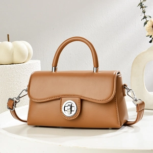 Detail of tan leather crossbody bag with silver twist lock on a minimalist marble surface