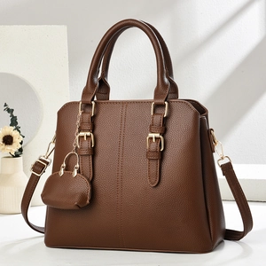 Close-up of dark brown lychee leather handbag with golden buckles and mini purse charm