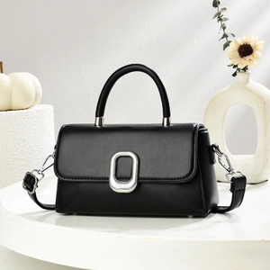 Classic black leather crossbody bag with silver oval buckle on a minimalist white display