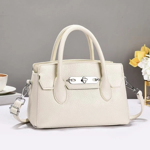 Detail of cream-colored lychee textured leather bag with silver twist lock and dual handles