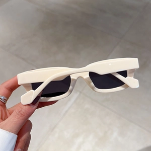 Detail view of stylish cream rectangular sunglasses held by hand with dark lenses
