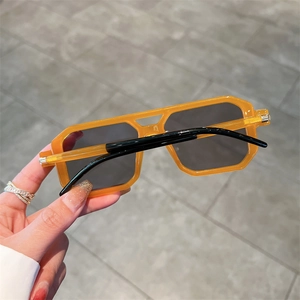 Detail of bright orange geometric square sunglasses held by hand with dark grey lenses