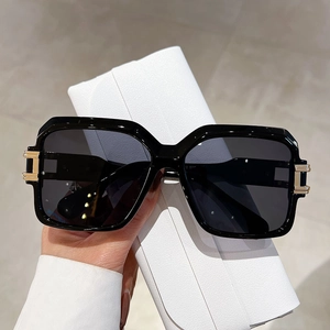 Detail of square sunglasses with gold H-metal hinge next to white leather case