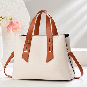 Detail of cream lychee texture tote bag with brown leather handles and gold metal accents