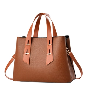 Brown leather tote bag with wide handles and gold metal accents on a white background
