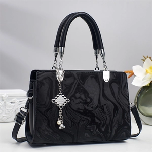 Detail of black crossbody bag with marble texture, silver chain, and pearl pendant accent