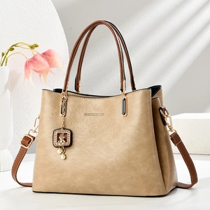 Vintage beige crossbody bag with gold bear charm and top handles on a sunny background