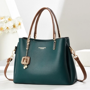 Deep green pebble leather handbag with brown handles and a gold pearl charm on white decor