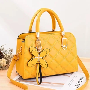 Yellow quilted leather handbag with floral charm and shoulder strap shown at 45 degrees