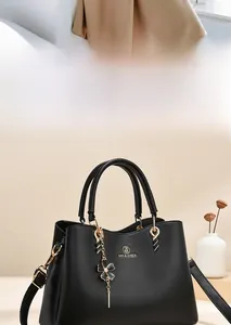 Detail of black matte handbag featuring gold SHI & ZHEN logo and flower metal pendant charm