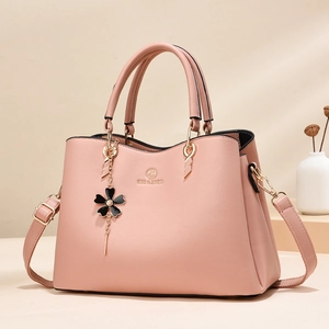 Pink luxury faux leather handbag with top handles and floral pendant on beige background
