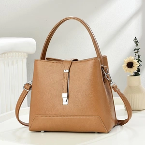 Trapezoidal brown pebble leather handbag with top handle and crossbody strap in elegant setting