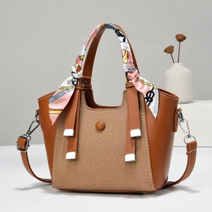 Brown leather handbag with woven panel and floral scarf detail on white table