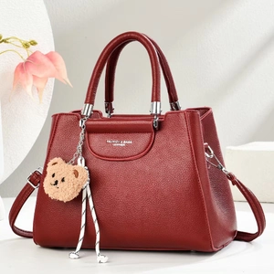 Close-up of burgundy lychee grain handbag with bear pendant and woven rope detail