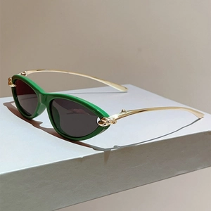 Detailansicht der grünen Cat-Eye-Sonnenbrille mit goldenen Metallbügeln auf grauem Ständer