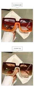 Close-up of oversized square sunglasses in orange and beige with metallic rivets detail