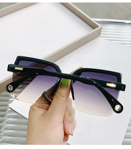 Detail of square oversized black sunglasses with gradient purple lenses and gold accents
