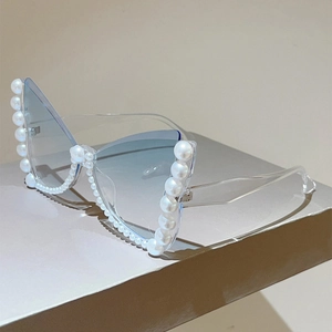 Detail view of pearl-embellished cat-eye sunglasses with blue gradient lenses on a stand