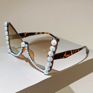 Detailed view of tortoiseshell cat-eye sunglasses featuring white pearl trim and brown lenses