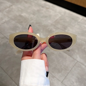 Retro oval sunglasses with cream white thick frames and black lenses held in hand