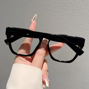 Detail of oversized black cat-eye anti-blue light glasses held by hand in a minimalist setting