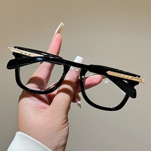 Detail of glossy black cat-eye glasses frame with golden arrow patterned metal accents