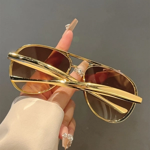 Detail of aviator sunglasses featuring polished gold metal double bridge and brown lenses