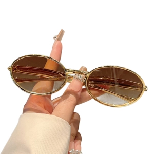 Lunettes de soleil ovales rétro avec monture dorée et verres bruns tenues à la main