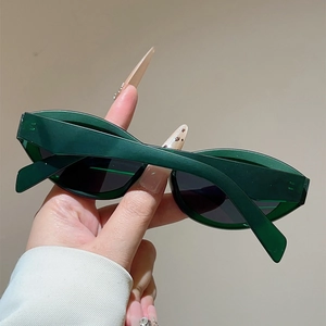 Detail of dark green cat-eye sunglasses with thick frame and gray lenses held by hand