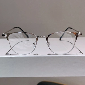 Detailed close-up of silver semi-rimless metal glasses frames on a minimalist white stand