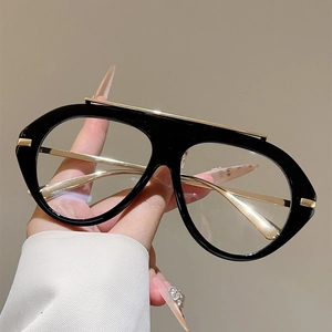 Detail of oversized black and gold pilot glasses held by hand against a warm background