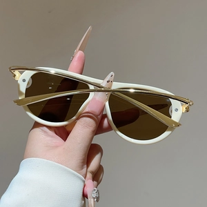 Detail einer cremefarbenen Sonnenbrille mit glänzend goldenen Bügeln und braunen Gläsern
