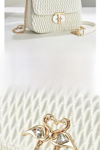 Detail of white quilted handbag featuring twin swan gold buckle with heart crystal accents