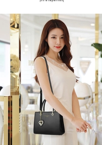 Close-up of black leather tote bag with heart-shaped crystal pendant and gold lettering