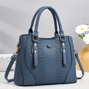 Borsa tote blu con motivo a coccodrillo, doppi manici e tracolla su una scrivania