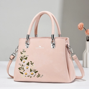 Pink leather tote bag with floral embroidery and silver handles on a minimalist background