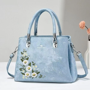 Detail view of light blue tote bag featuring fine floral embroidery and silver hardware