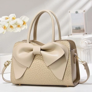 Detailed view of beige crocodile embossed handbag featuring a large elegant bow decoration