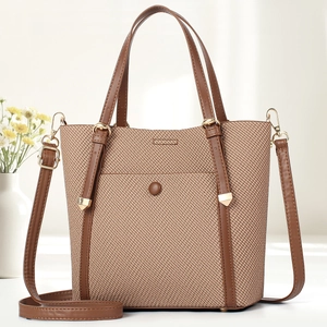 Brown woven texture tote bag with leather straps and adjustable shoulder strap on white desk