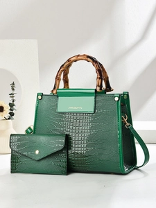 Close-up of emerald green crocodile embossed handbag with dark bamboo handles and matching wallet