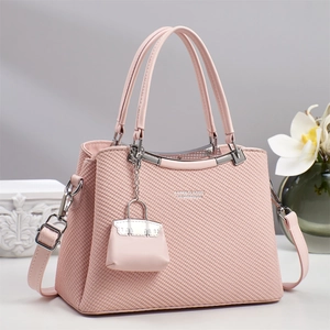 Detail of pink crossbody bag with woven texture, metal logo, and mini bag charm