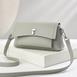 Minimalist light grey leather crossbody bag with adjustable strap on white stone base
