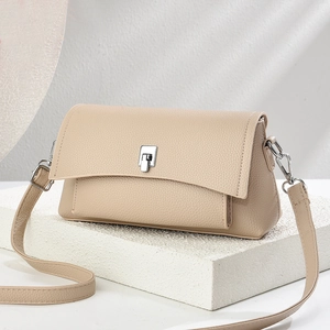 Beige pebble leather crossbody bag with silver twist lock on a minimalist white stone pedestal