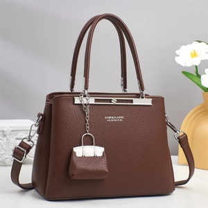 Close-up of brown lychee leather handbag with brand logo and mini charm accessory