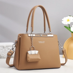 Detail of camel leather handbag with brand lettering and mini bag pendant accessory