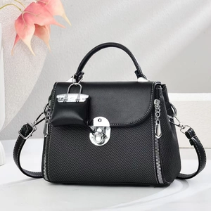 Détail du sac bandoulière noir avec fermoir argenté, texture diagonale et petit pendentif