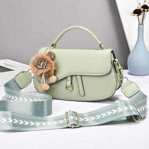Detail of light green leather saddle bag with patterned strap and cute plush charm