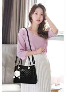 Detail of black tote bag with letter texture, shoulder strap and white fur ball charm