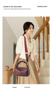 Detail of burgundy leather satchel with cloud handle and wide fabric strap on a model